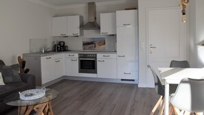 A compact kitchen with white cabinets, a built-in oven, and a coffee maker. - Apartment oasis in Dünenhof (St. Peter-Ording)