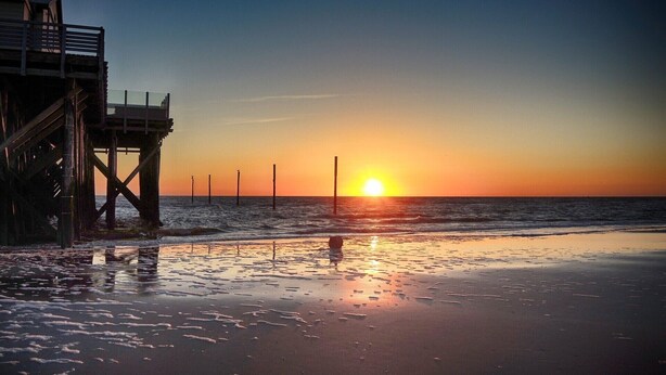 A pier extending into the ocean with the sun setting in the background. - Apartment oasis in Dünenhof (St. Peter-Ording)