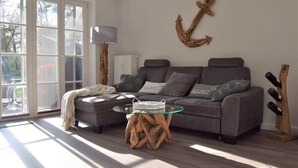 A living room with a grey sofa, a glass coffee table, and a wooden side table. - Apartment oasis in Dünenhof (St. Peter-Ording)