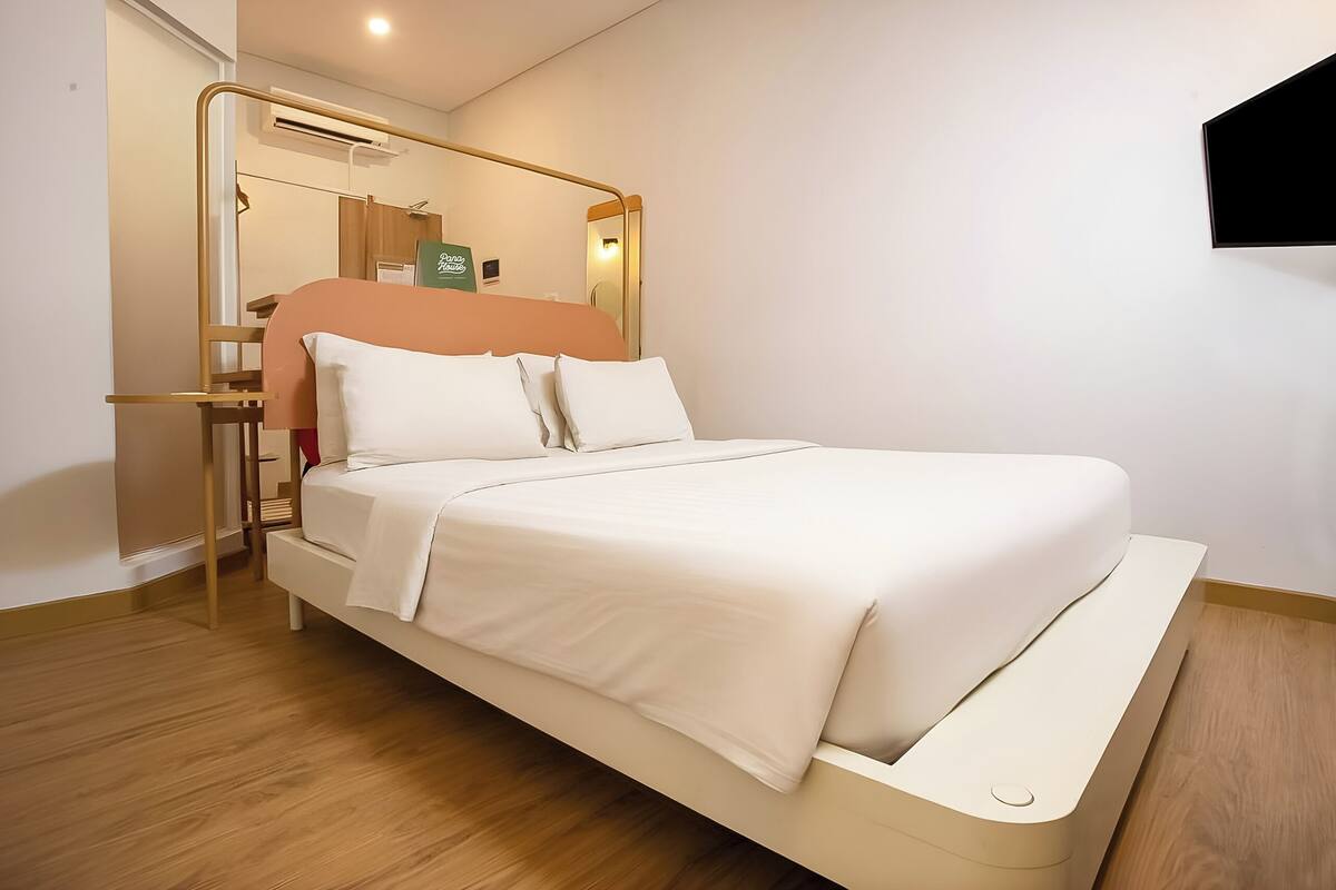 A modern hotel room with a bed, a bedside table, a mirror, and a wall-mounted TV.