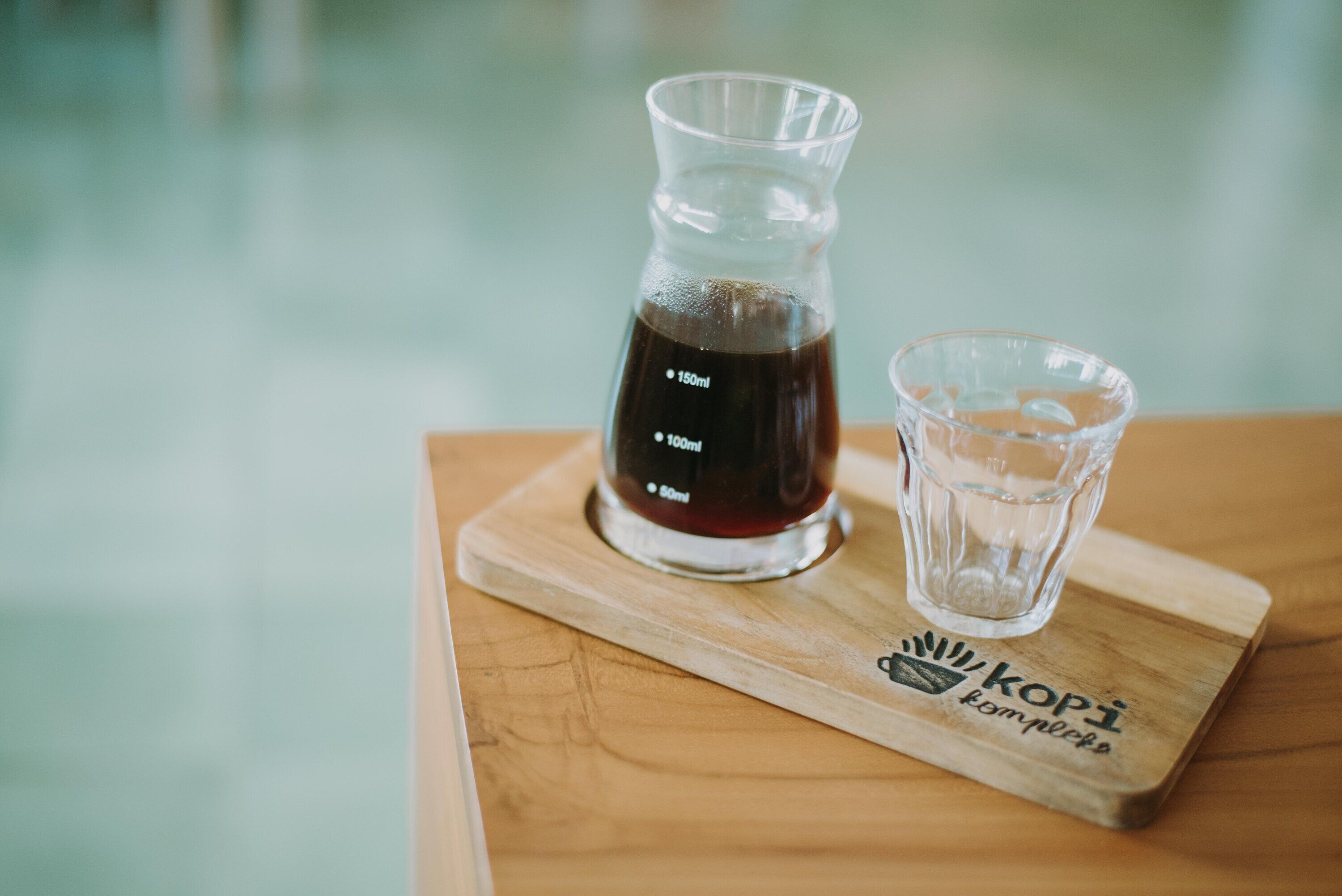 A glass carafe and a glass on a wooden board with a logo.