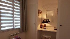 Une chambre d’hôtel avec un lit, un petit tabouret, un bureau avec une lampe et un miroir.