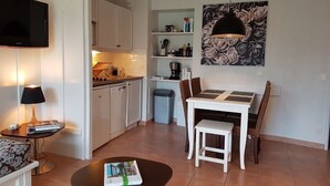 Un espace de vie compact comprenant un coin cuisine, un coin repas et un téléviseur fixé au mur.