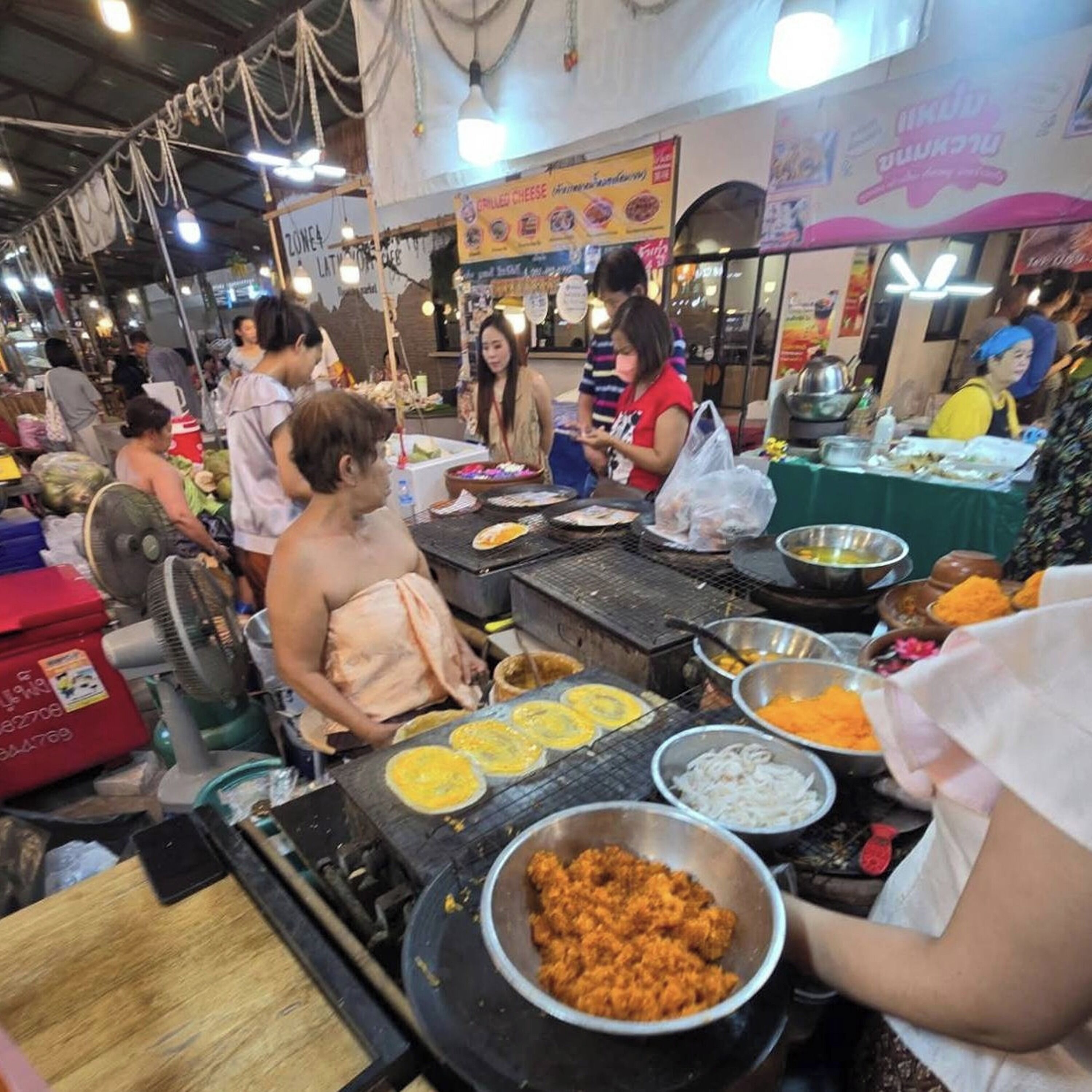 A bustling food market with various food stalls and cooking equipment.