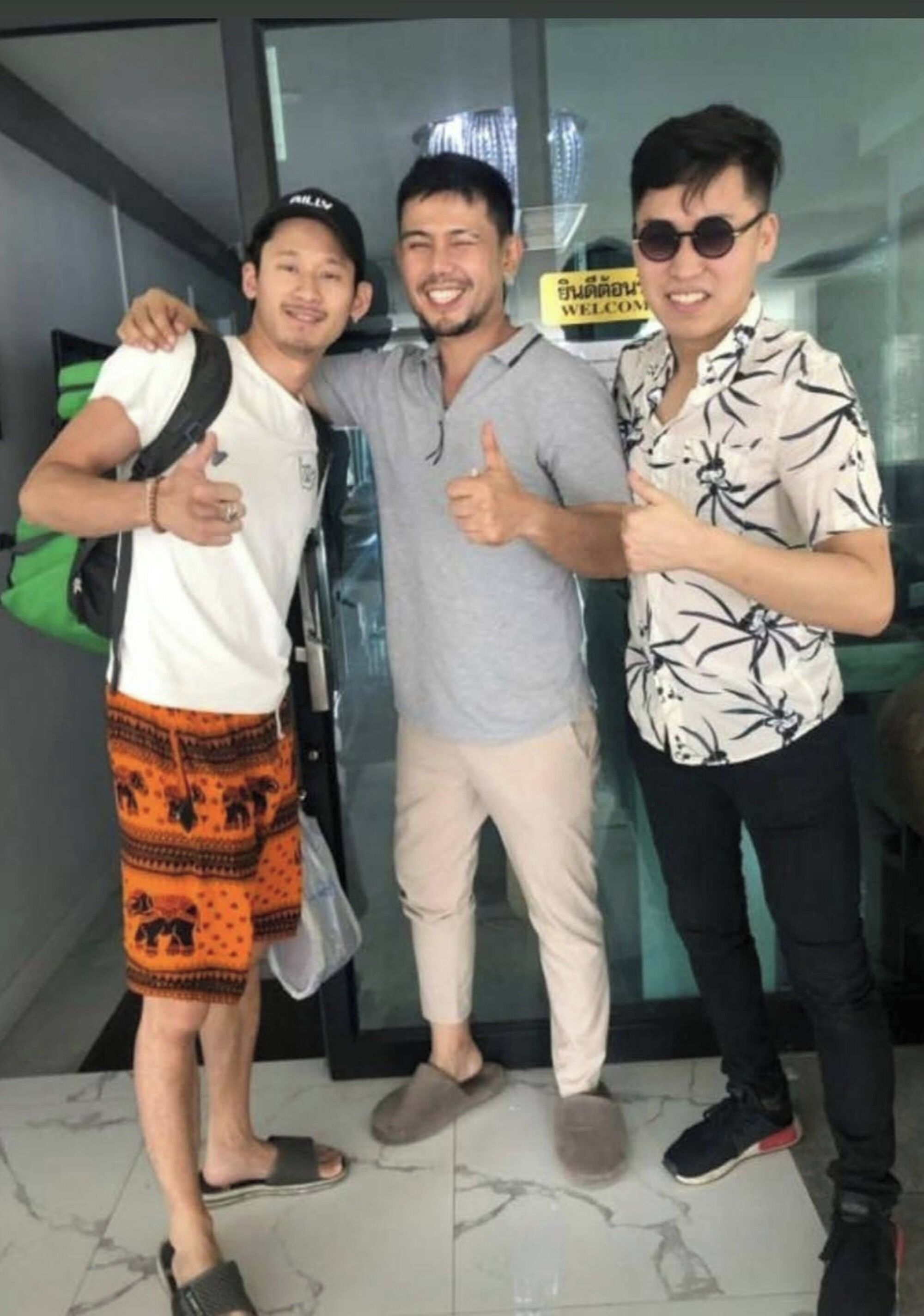 Three people posing in a modern indoor setting with a glass wall and a 'Welcome' sign.