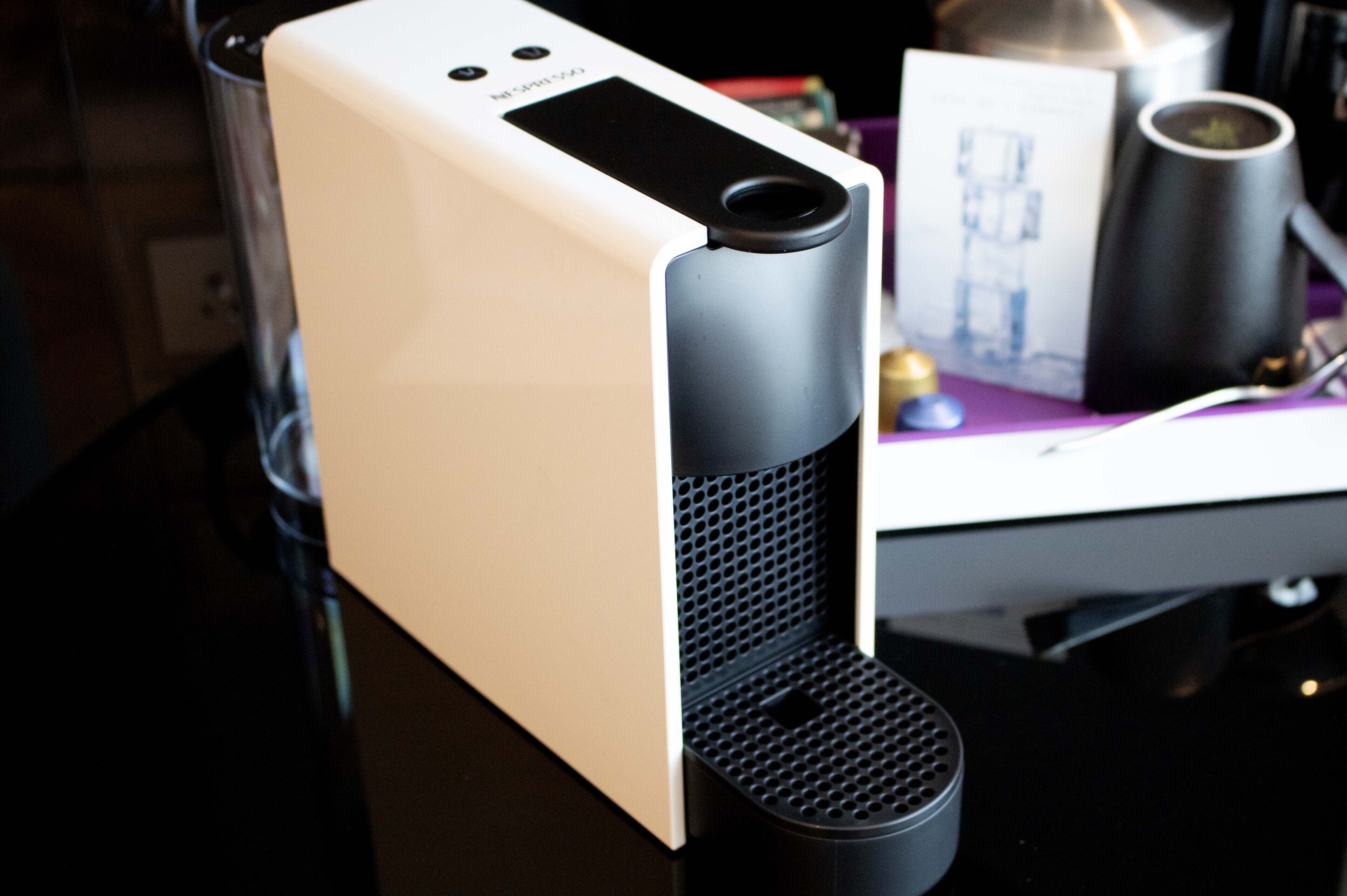 A white and black speaker with a perforated front panel, placed on a table with a purple surface.