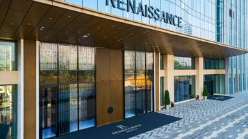 Une entrée d’hôtel moderne avec une façade en verre, un auvent en bois et un chemin piétonnier au motif en chevrons.