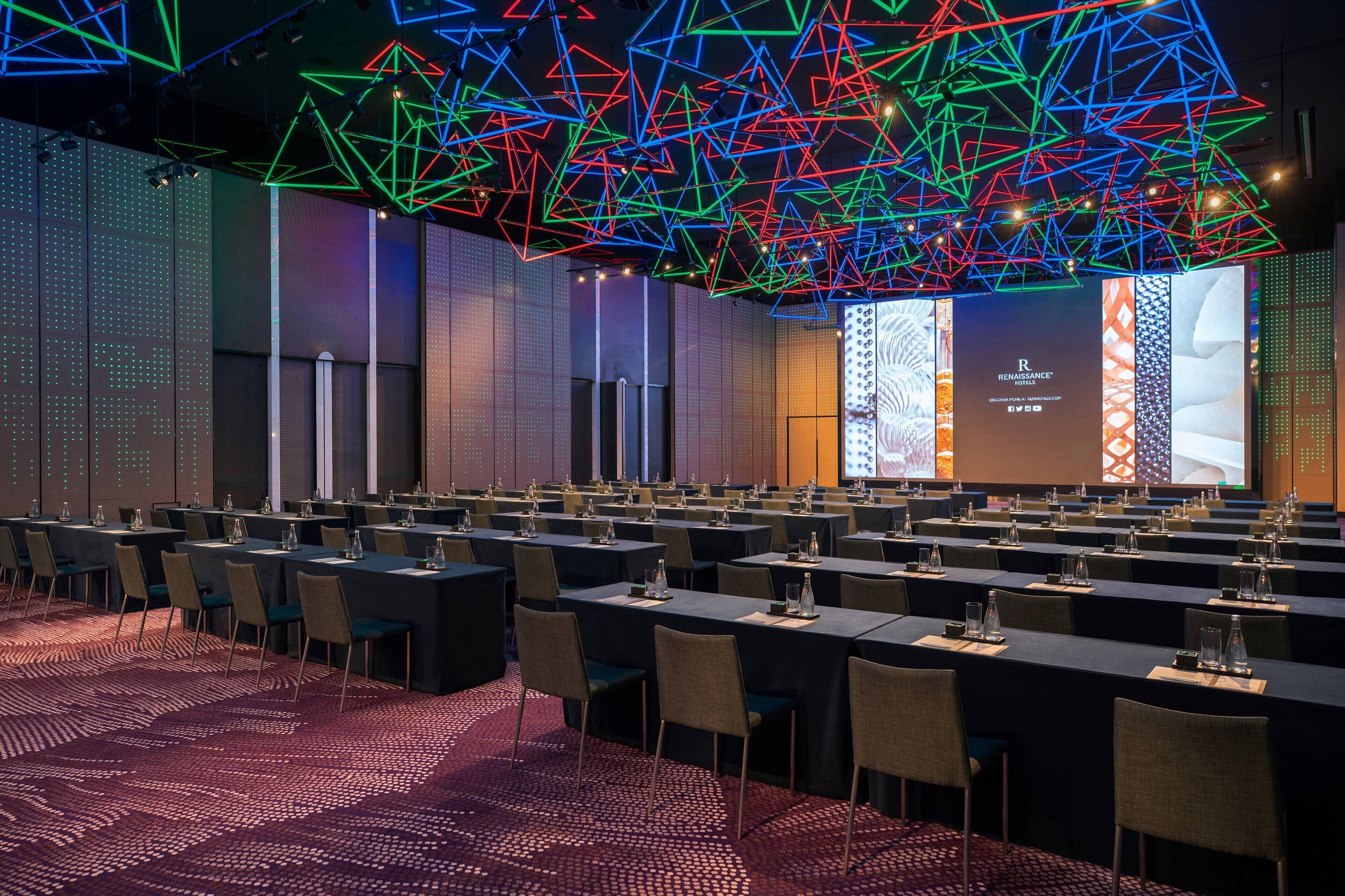 A conference room with tables, chairs, and a large screen for presentations.
