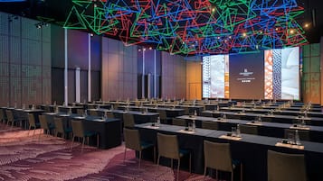 Un salón de conferencias con mesas, sillas y una pantalla grande para presentaciones.