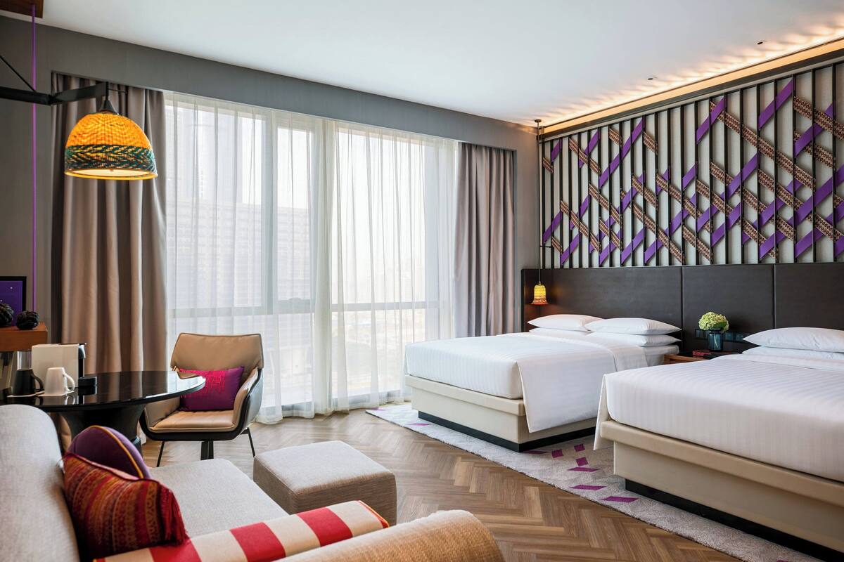 A hotel room with two beds, a sofa, a dining table, and a large window with curtains.