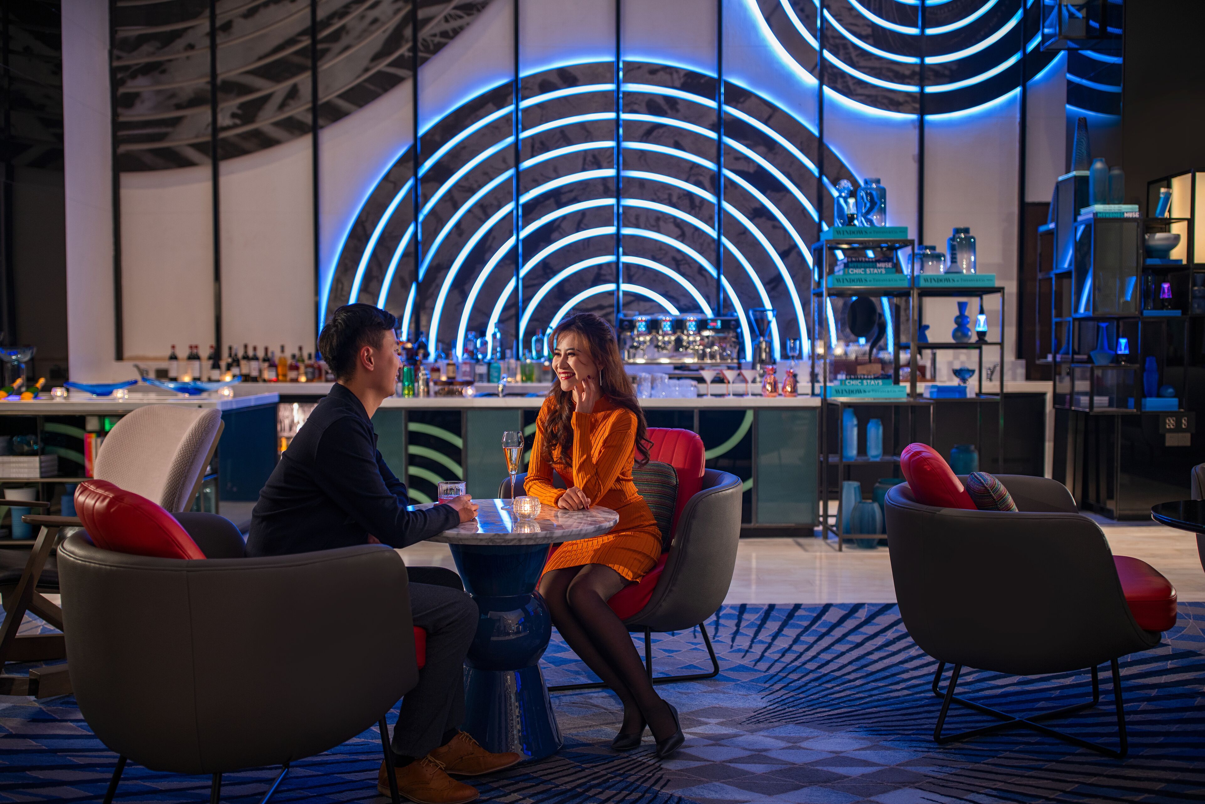 A modern bar area with a circular light design on the wall, bar stools, and a round table.