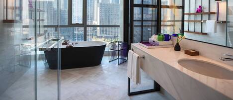 A modern bathroom with a freestanding bathtub, a large mirror, and a view of the cityscape through large windows.