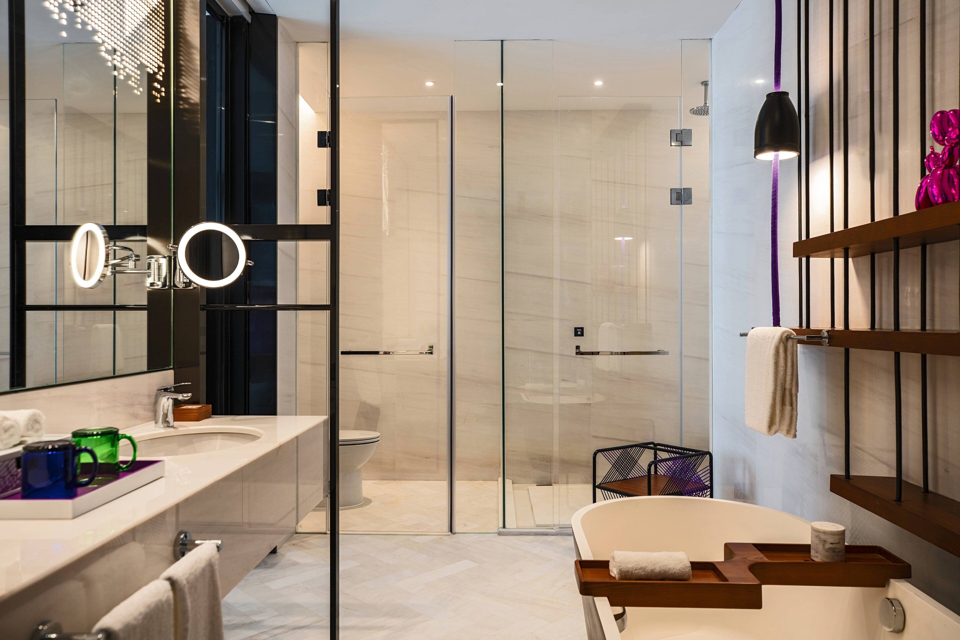 A modern bathroom with a glass-enclosed shower, a large mirror with integrated lighting, and a wooden vanity with a marble countertop.