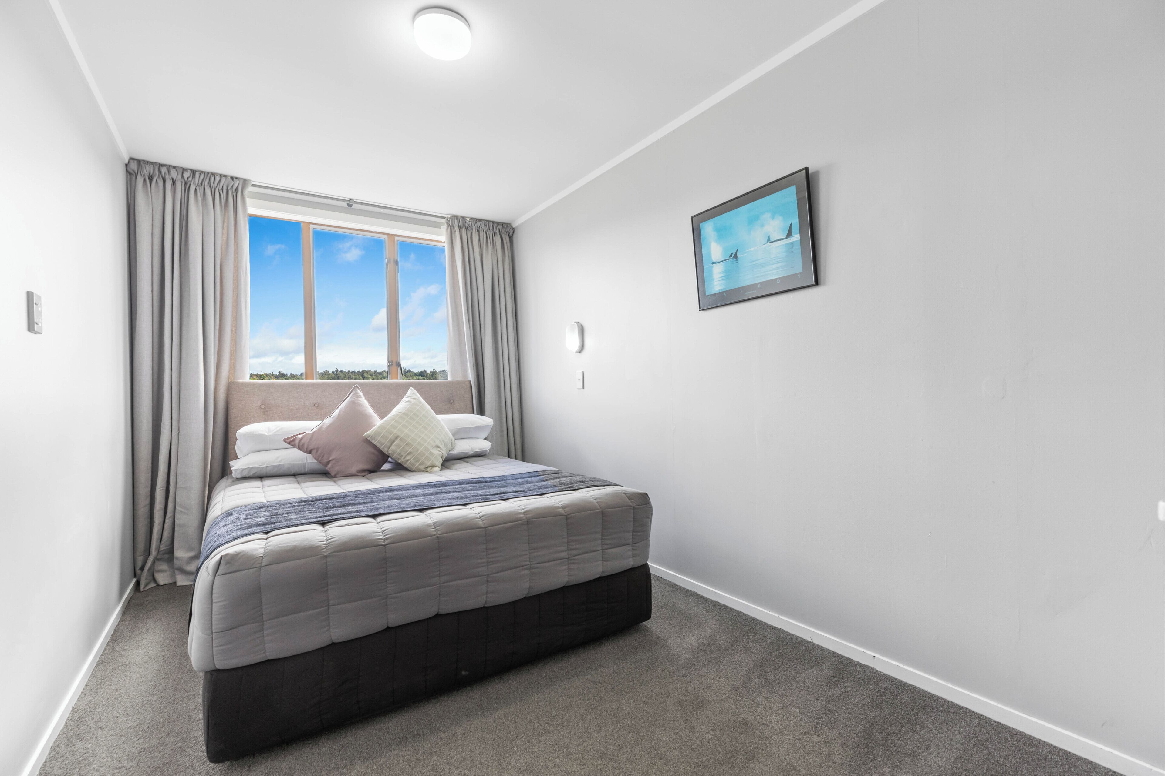 A bedroom with a bed, curtains, a window with a view, and a framed picture on the wall.
