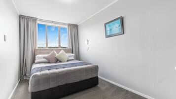 A bedroom with a bed, curtains, a window with a view, and a framed picture on the wall.