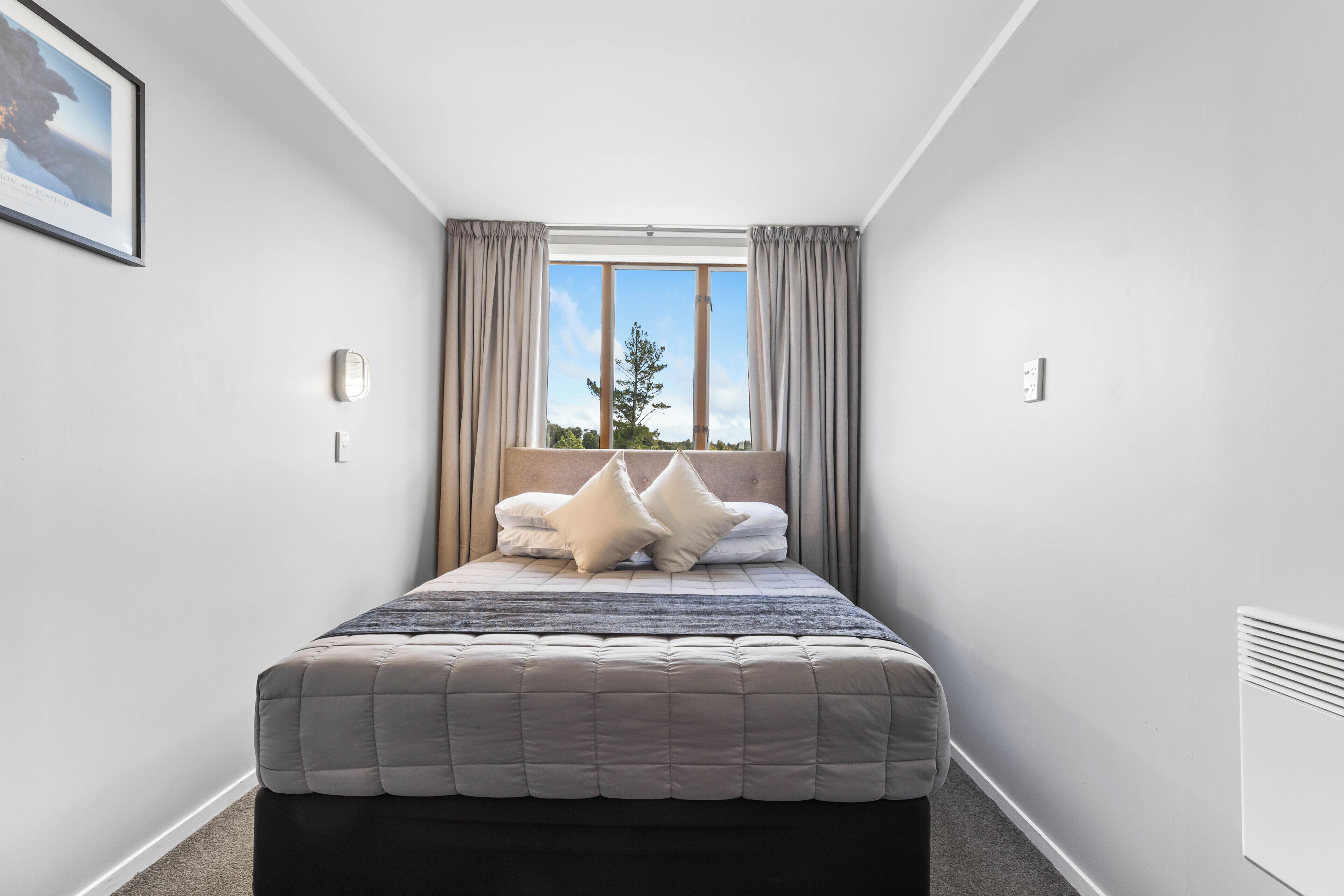 Un dormitorio con cama, cortinas, ventana y radiador.