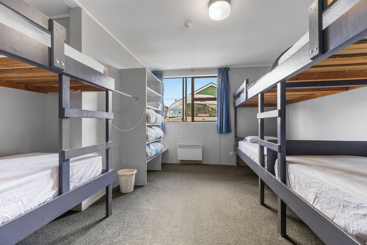 A bunk room with three bunk beds, a window with curtains, and a radiator.