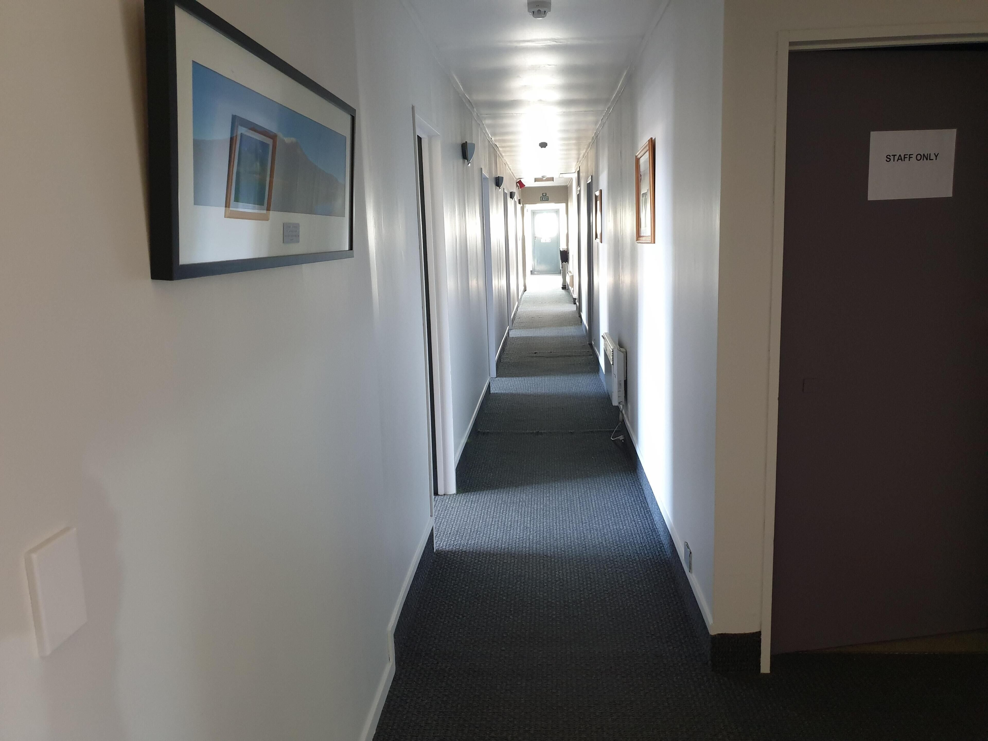 A long, narrow hallway with framed pictures on the walls, a carpeted floor, and a door labeled "STAFF ONLY" on the right.
