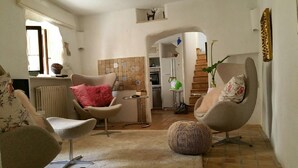 A living room with two armchairs, a small table, and a radiator. There is a kitchen area with a refrigerator and a staircase leading to an upper floor. - Town house Sant Llorenc, east coast Mallorca, 15 minutes to the beach (Sant Llorenc)