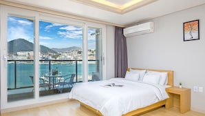 Une chambre dotée d’une grande porte-fenêtre coulissante donnant sur un balcon avec vue sur une ville côtière et des montagnes.
