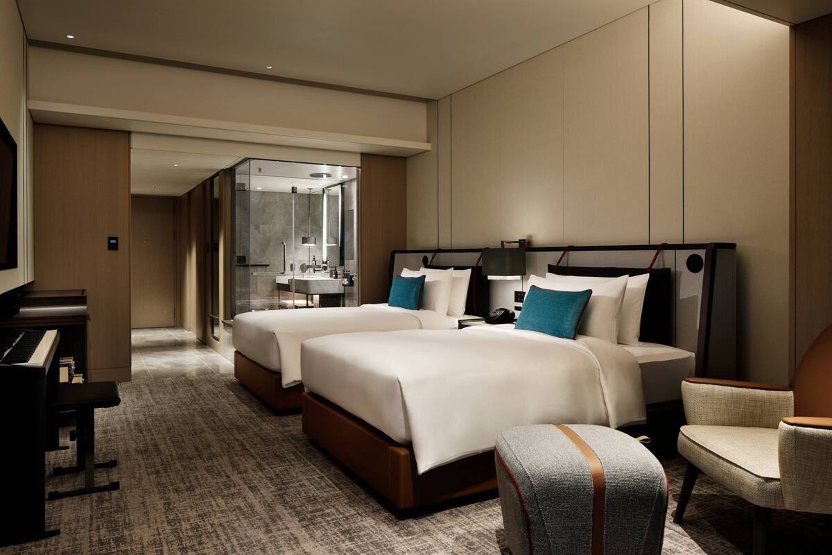 A hotel room with two beds, a piano, a desk, and a chair.