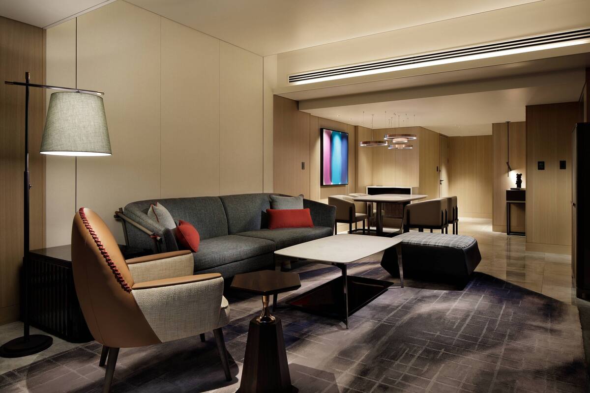 A modern living room with a sofa, armchairs, a coffee table, and a floor lamp. There is a dining area with a table and chairs in the background.