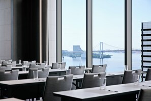 A restaurant with tables and chairs arranged for dining, large windows offering a view of a bridge and water.