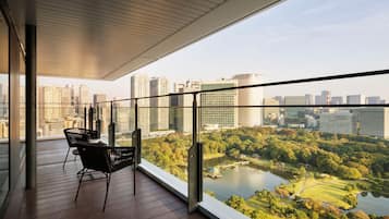 Un balcón moderno con vista a la ciudad, piso de madera y sillas negras.