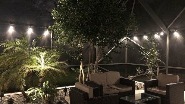 An outdoor seating area with wicker furniture and potted plants, under a covered structure with string lights. - Charming private pool home 3br/ 2 bath (West Palm Beach)