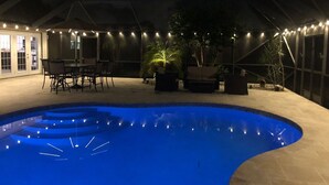 A covered outdoor swimming pool area with a curved pool, seating arrangements, and ambient lighting. - Charming private pool home 3br/ 2 bath (West Palm Beach)