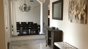 A hallway with a dining area in the background, a chandelier, a bench, and a mirror on the wall. - Charming private pool home 3br/ 2 bath (West Palm Beach)