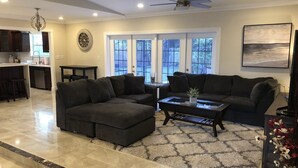 A modern living room with a sectional sofa, a coffee table, and a dining area with a kitchen in the background. - Charming private pool home 3br/ 2 bath (West Palm Beach)
