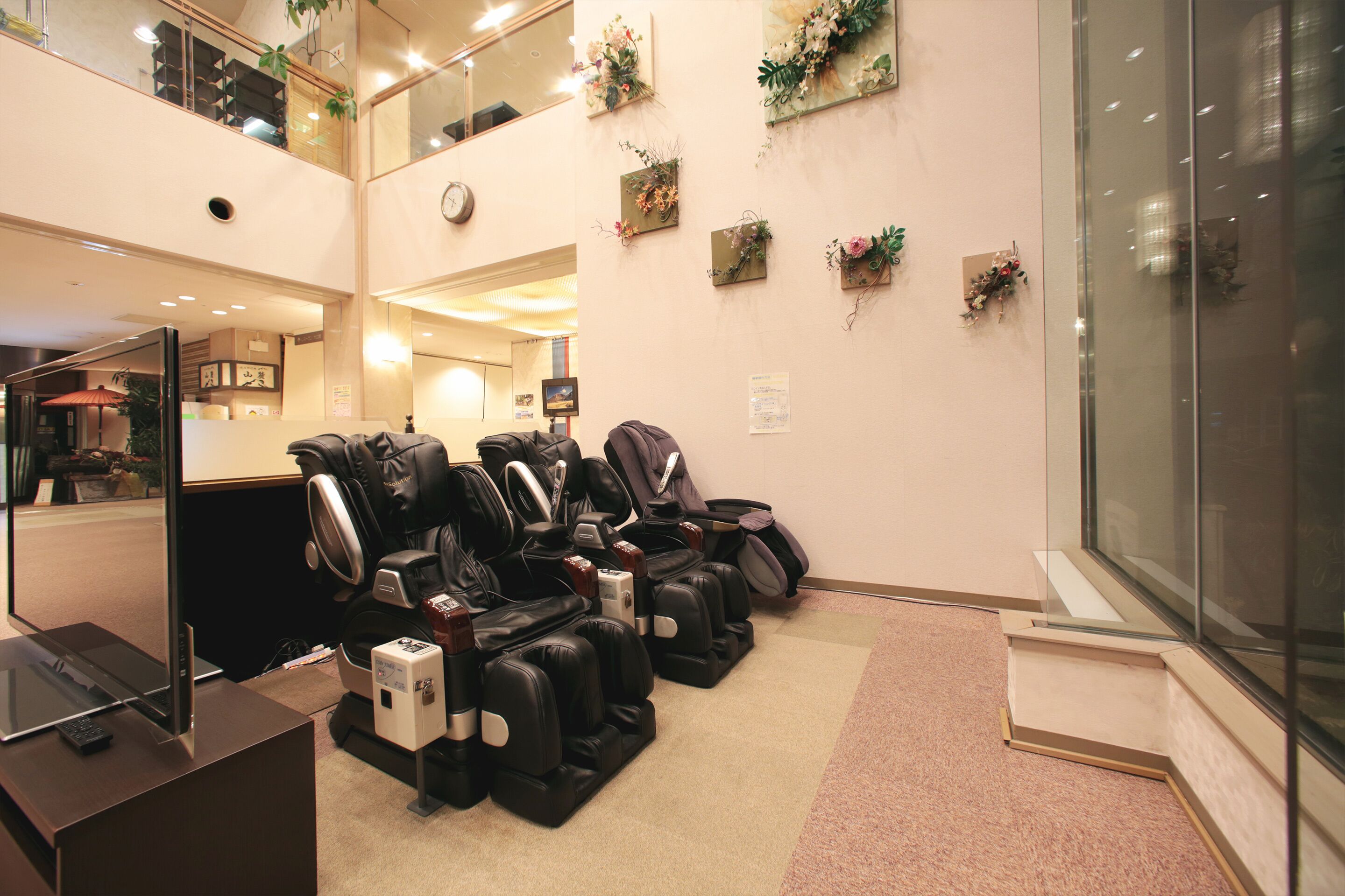 A massage therapy room with several massage chairs, a television, and a small desk with a remote control.