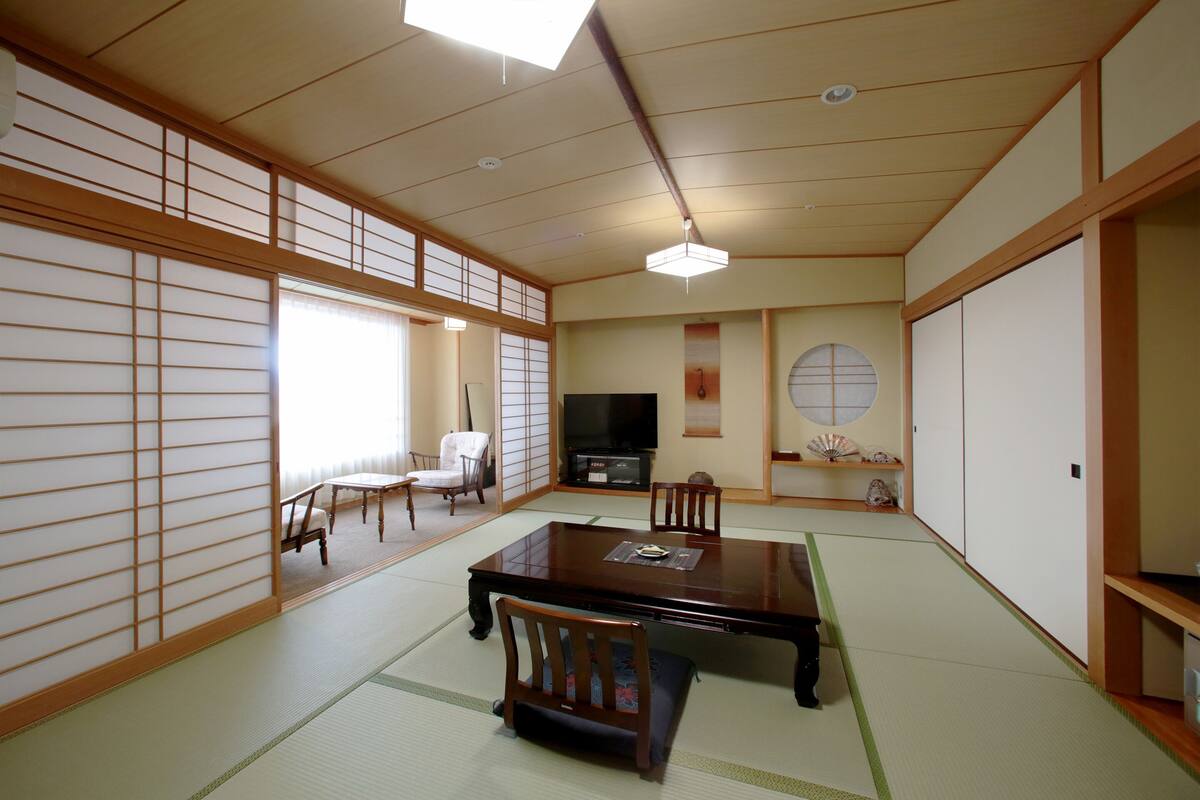 A traditional Japanese room with tatami flooring, a low table, chairs, a television, and sliding doors.