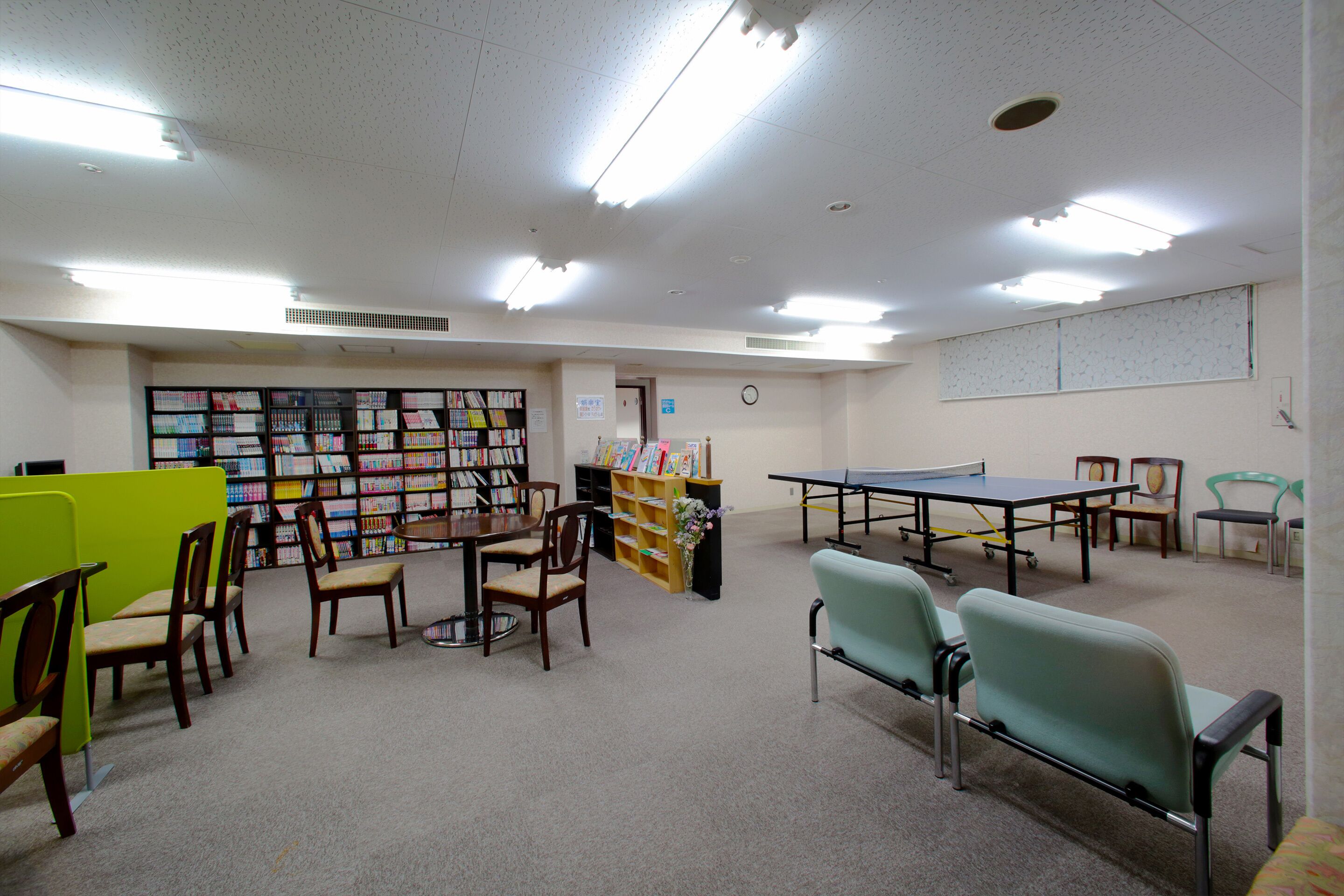 A library with bookshelves, chairs, a table, and a ping pong table.