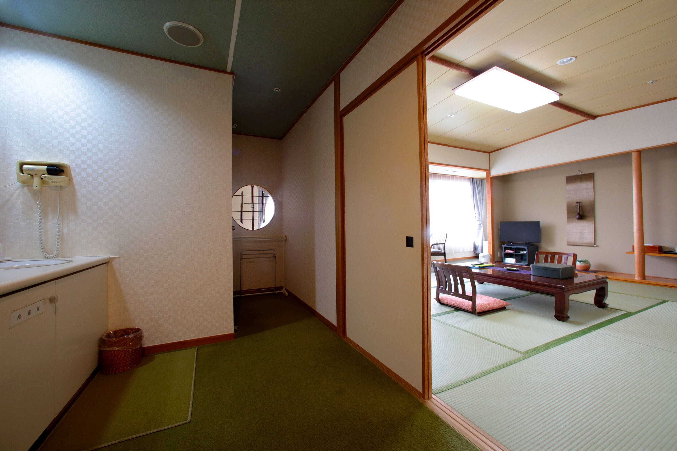 Una habitación japonesa tradicional con suelo de tatami, una mesa baja, un televisor y una cama futón.