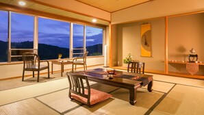 Een traditionele Japanse kamer met tatami vloerbedekking, een lage houten tafel en stoelen. Grote ramen bieden uitzicht op het omliggende landschap.