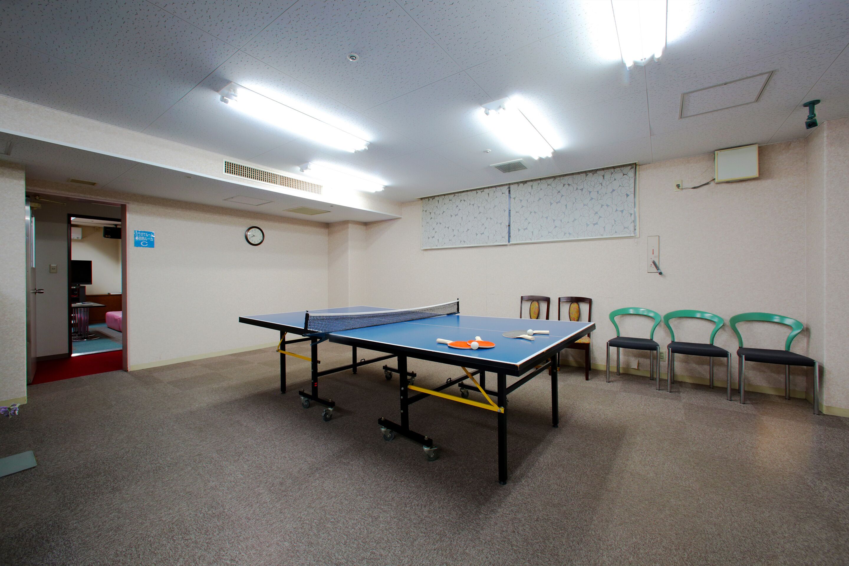 A room with a ping pong table, chairs, and a clock on the wall.