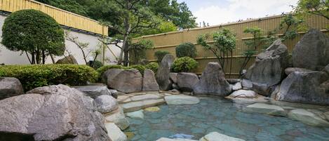 A traditional Japanese garden with a clear stone pond, large rocks, and neatly trimmed bushes.