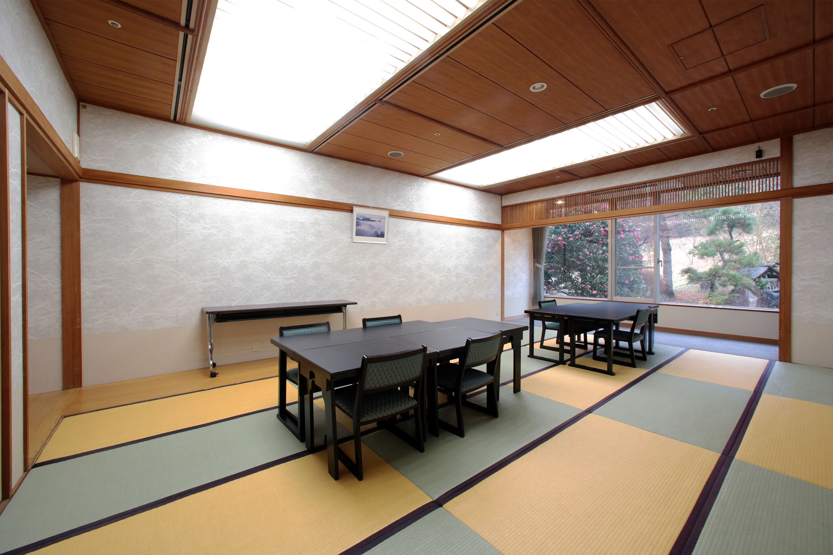 A traditional Japanese room with tatami flooring, wooden furniture, and a view through a large window.