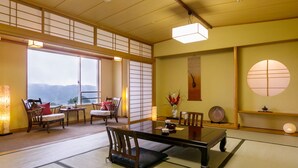 Een traditionele Japanse kamer met tatami vloeren, een lage tafel, stoelen, een groot raam met uitzicht en een schuifdeur.