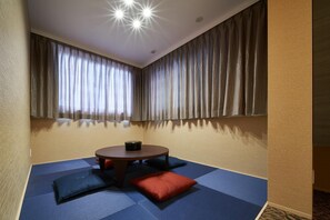 Ein Zimmer mit einer Sitzecke mit Tatami-Matten, einem runden Tisch und einer Deckenleuchte.
