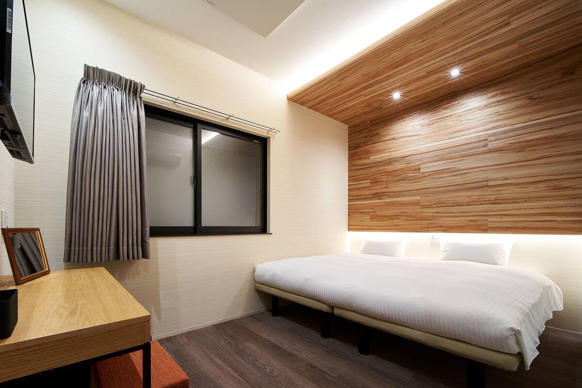 A modern bedroom with a wooden ceiling, a bed with white bedding, a bedside table, and a window with curtains.