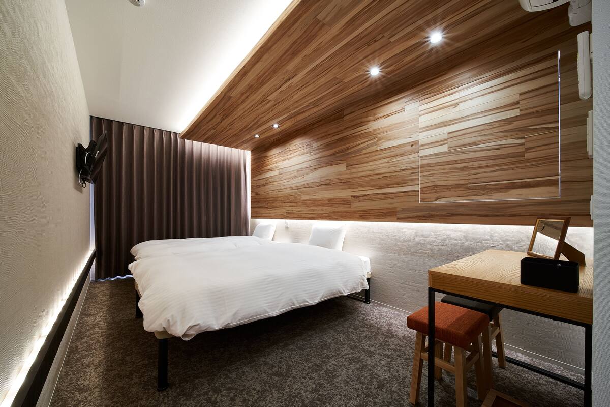 A modern hotel room with a bed, a desk with a chair, and a large window with curtains.
