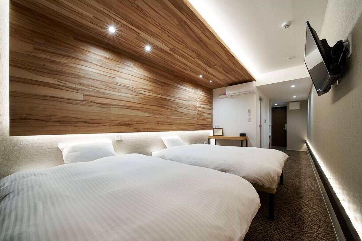 A hotel room with two beds, a wooden ceiling, a flat-screen TV mounted on the wall, and a carpeted floor.