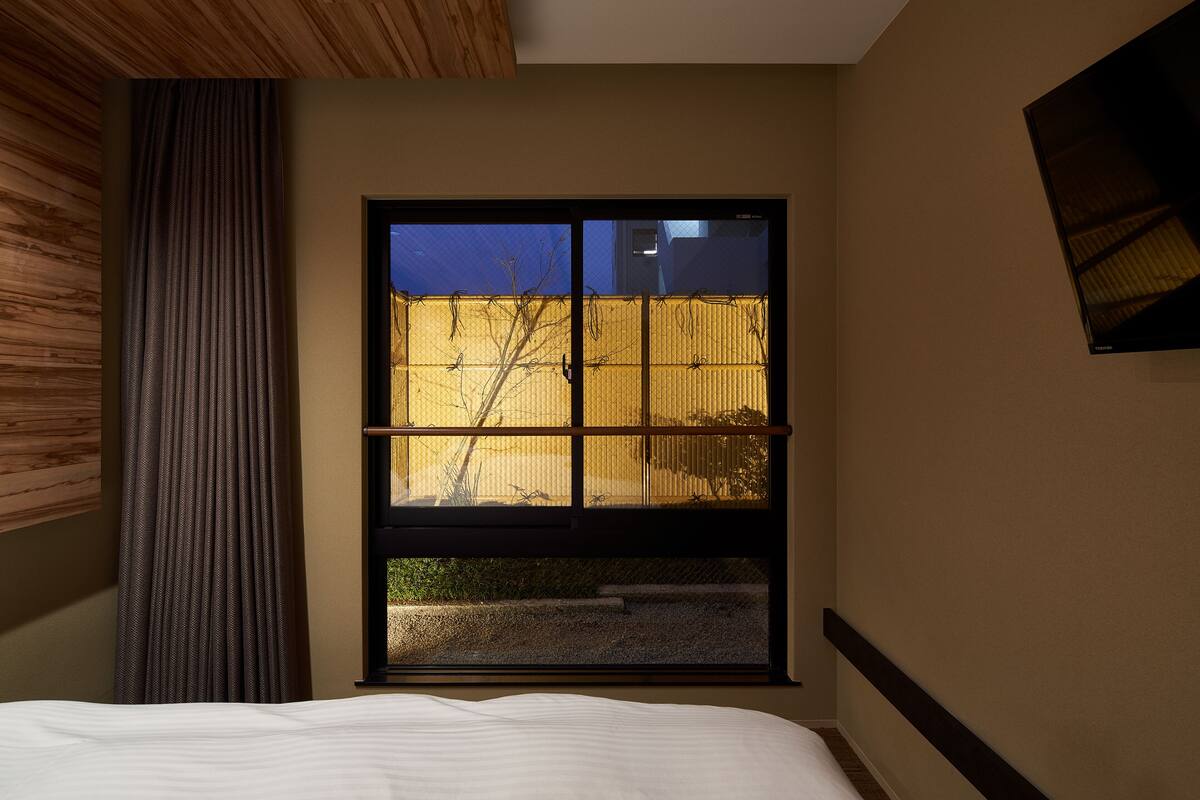 A bedroom with a large window, a bed, and a wooden ceiling.