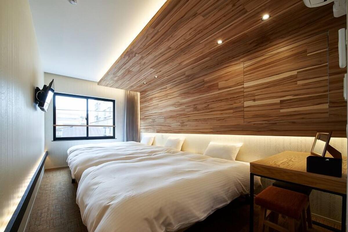 A modern hotel room with a large bed, a small desk, a chair, and a window with curtains.