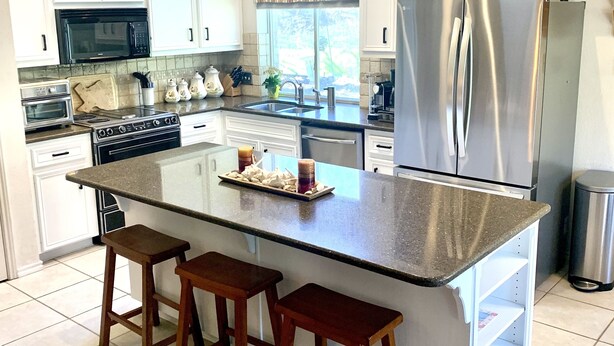 Una cucina moderna con mobili bianchi, un frigorifero in acciaio inox, una grande isola con sgabelli e una finestra con tende.