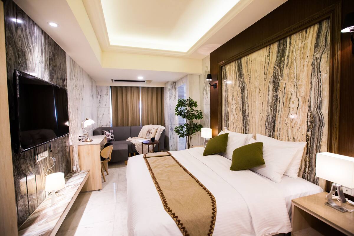 Una habitación de hotel con una cama grande, un escritorio, un televisor y una planta.