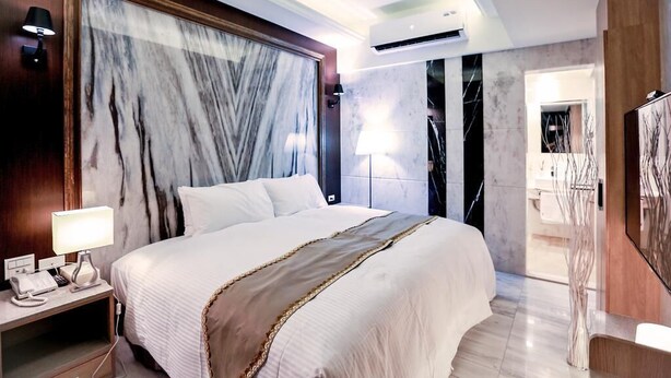 Ein Hotelzimmer mit einem großen Bett, einem Nachttisch mit Lampe, einem Schreibtisch mit Telefon und einem Spiegel.